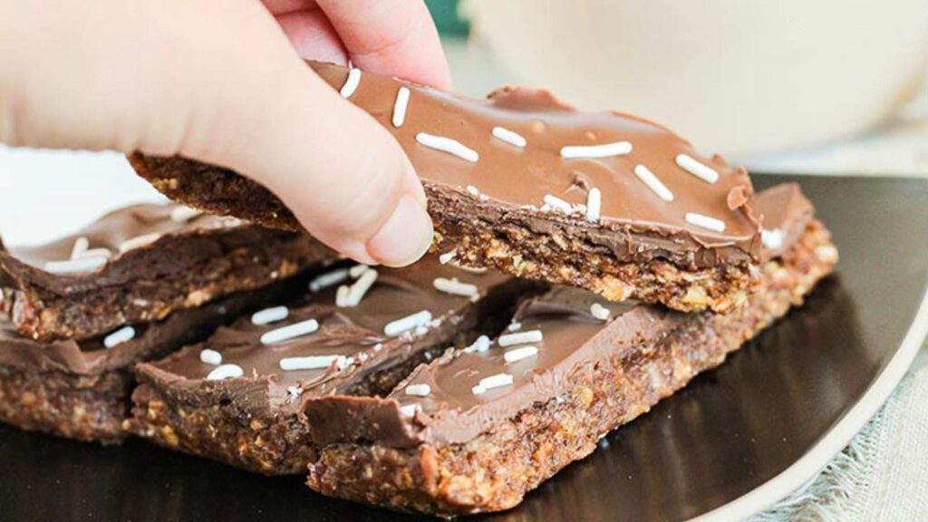 A hand reaches for a No Bake Pumpkin Protein Bar on a black plate.