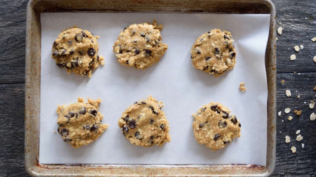 A parchment-lined cookie sheet with raw, Oatmeal Chocolate Chip Cookies sitting in two rows.