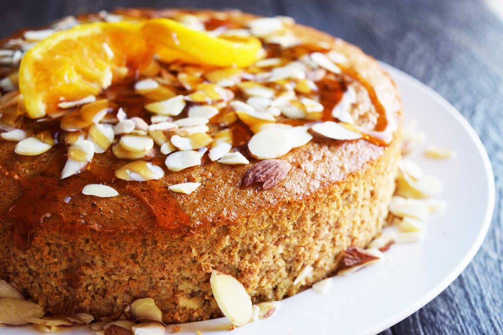 A front view of an Orange Almond Cake on a white plate, topped with sliced almonds and an orange slice twist.