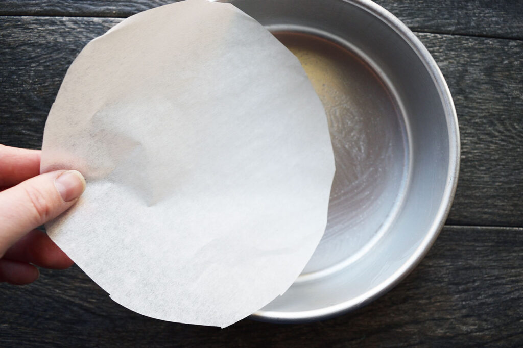 Placing cut parchment in the bottom of the cake pan.