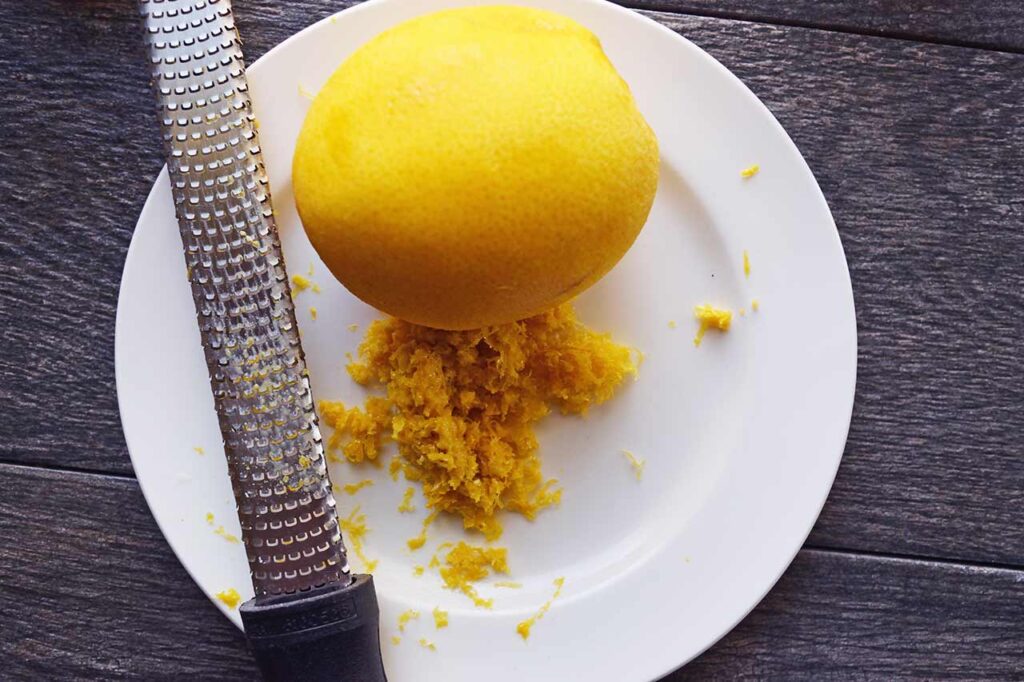 A zester, a zested orange and orange zest on a white plate.