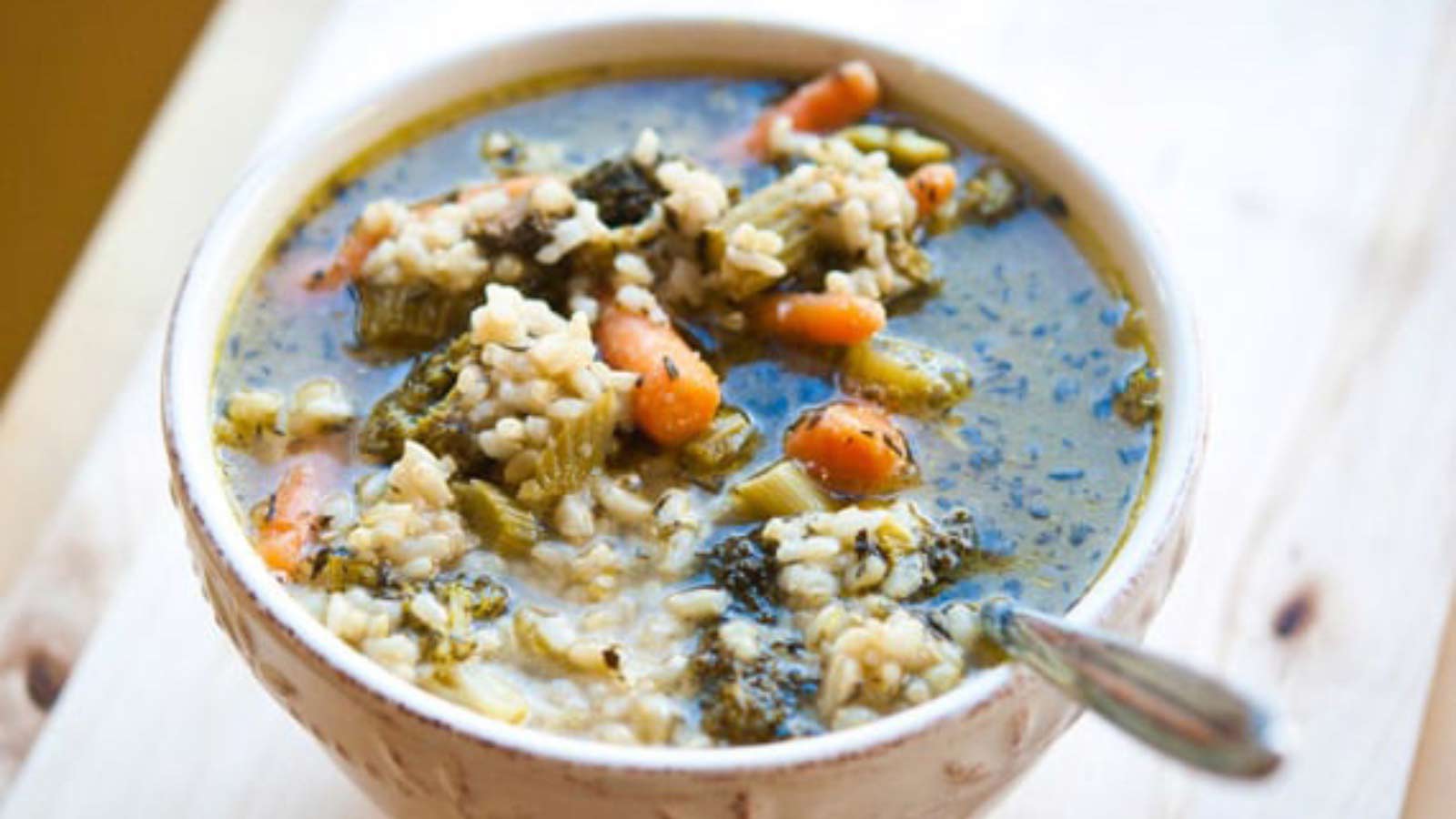 A bowl of Roasted Leftover Vegetable Tray Soup sits on a wooden counter with a spoon in it.