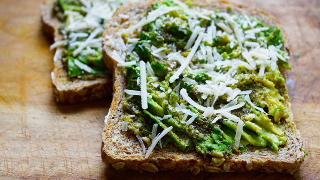 Two finished slices of Pesto Avocado Toast laying on a cutting board.