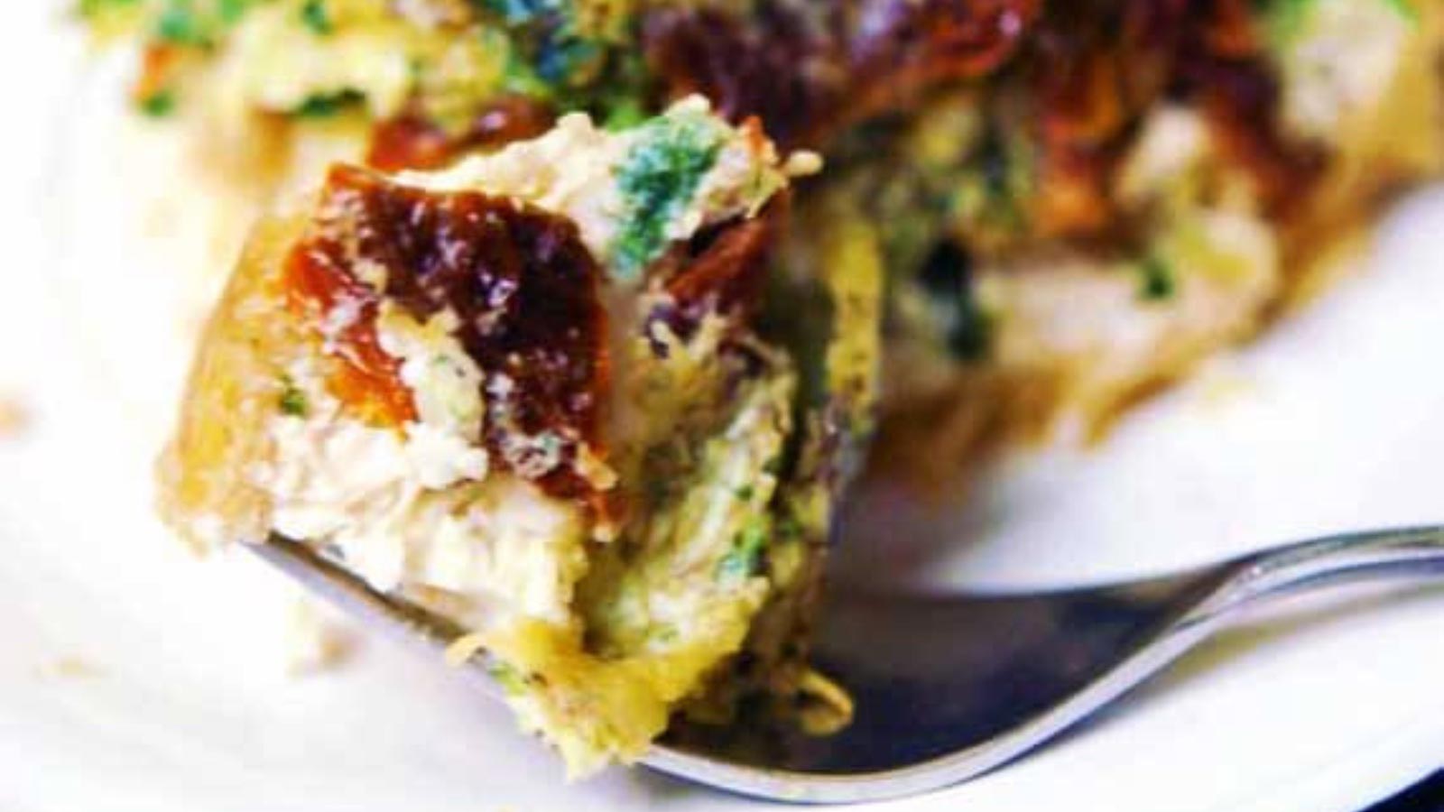 A closeup of a bit of pesto quiche on a fork, laying on a plate.