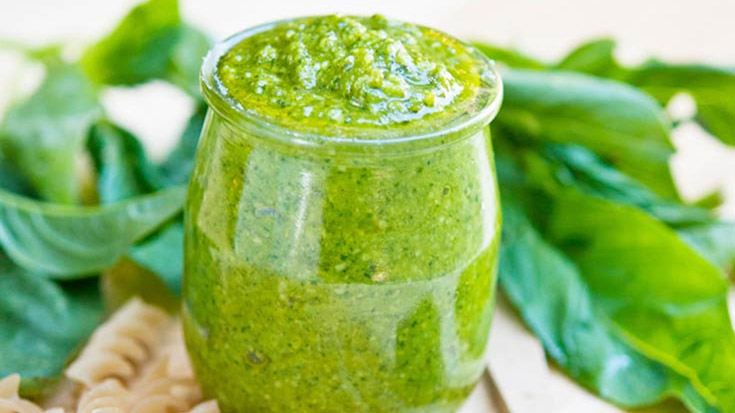 A small, glass jar filled with homemade basil pesto sauce.