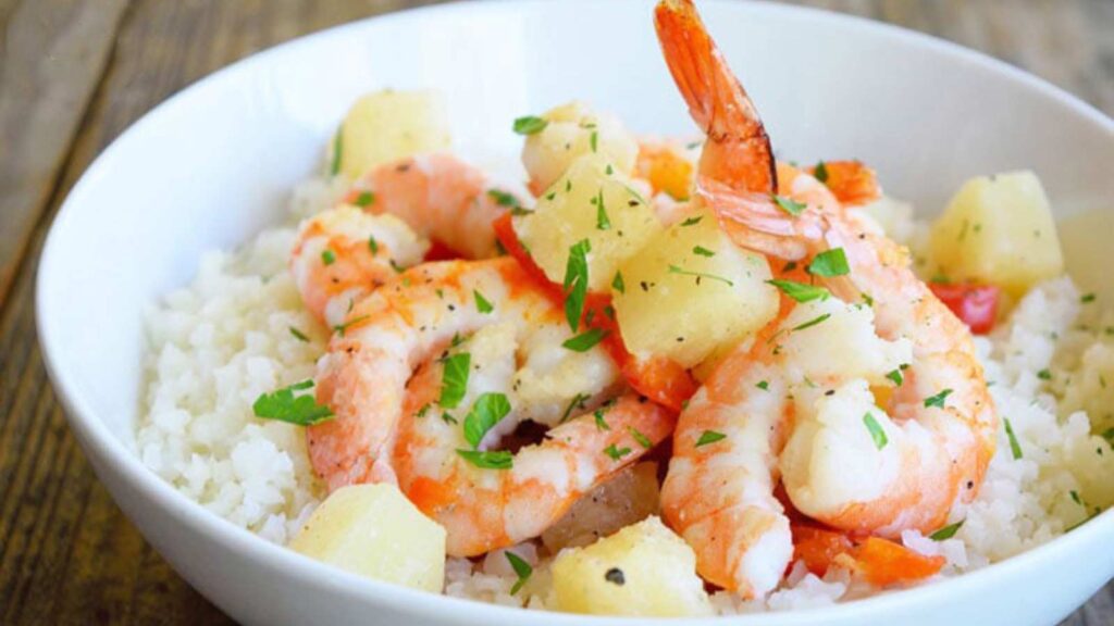 A white bowl filled with Sheet Pan Pineapple Shrimp served over riced cauliflower.