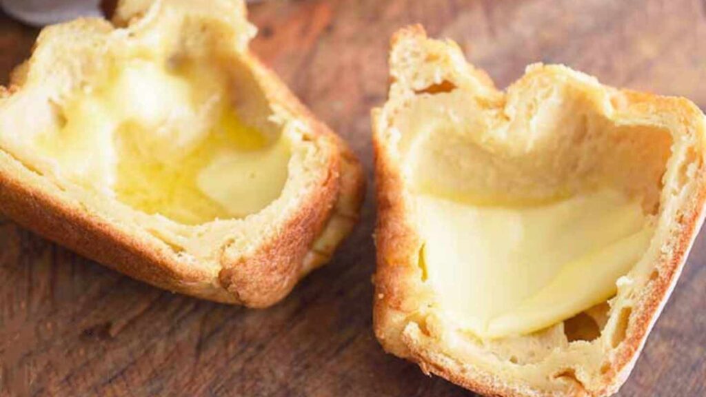 A popover sits cut in half with butter melting into it's middle.