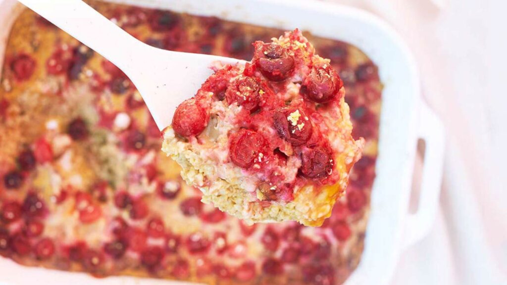 A spoons lifts a serving of Pumpkin Baked Oatmeal out of a white casserole dish.