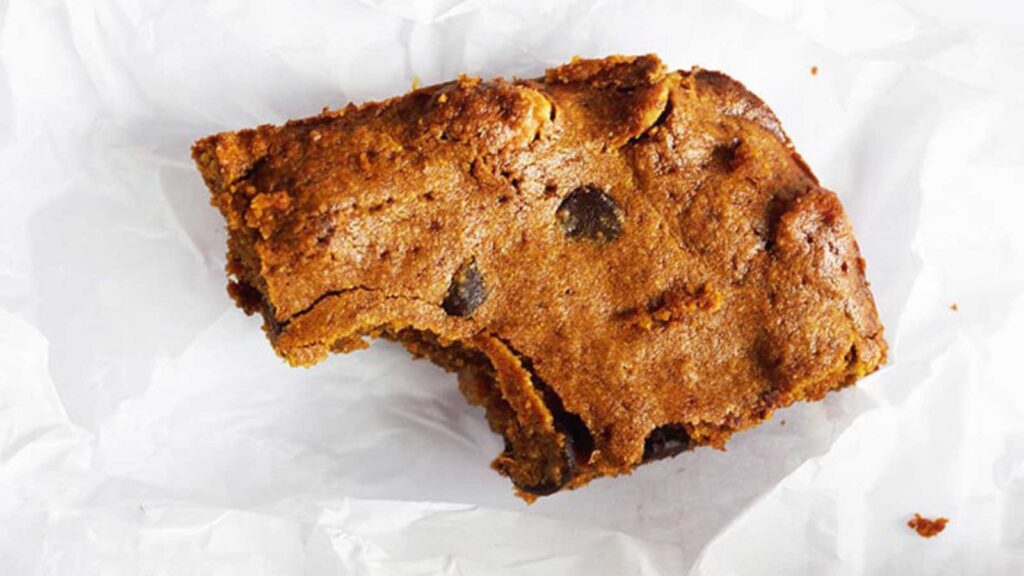 A single pumpkin blondie with a bite remove, laying on a white piece of parchment paper.