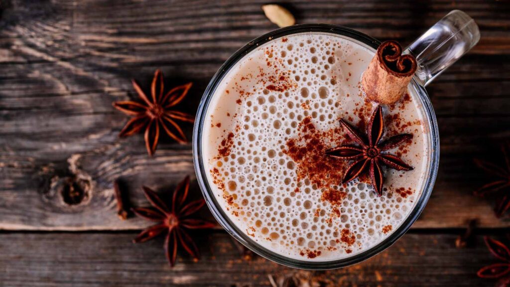 An overhead view of a glass mug filled with pumpkin spice chai latte garnished with a cinnamon stick and a star anise.