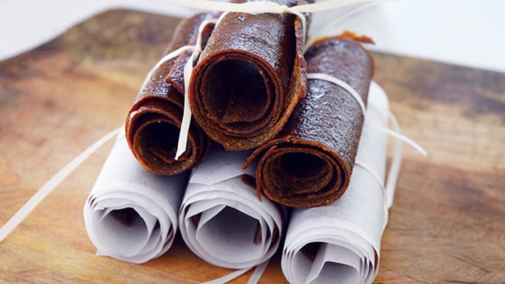 A stack of Pumpkin Fruit Leather rollups on a wooden cutting board.