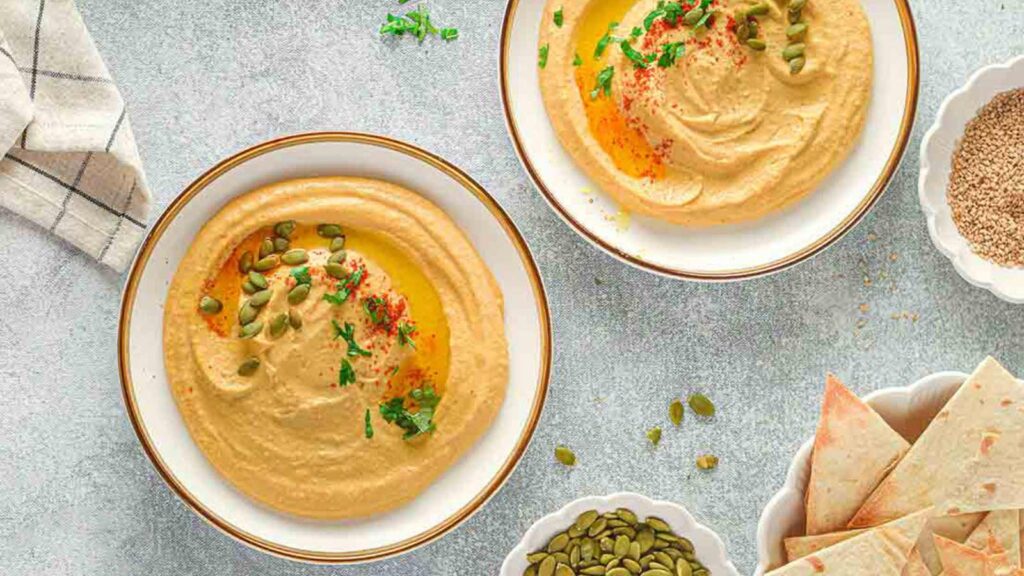 An overhead view of two bowls of pumpkin hummus on a table.