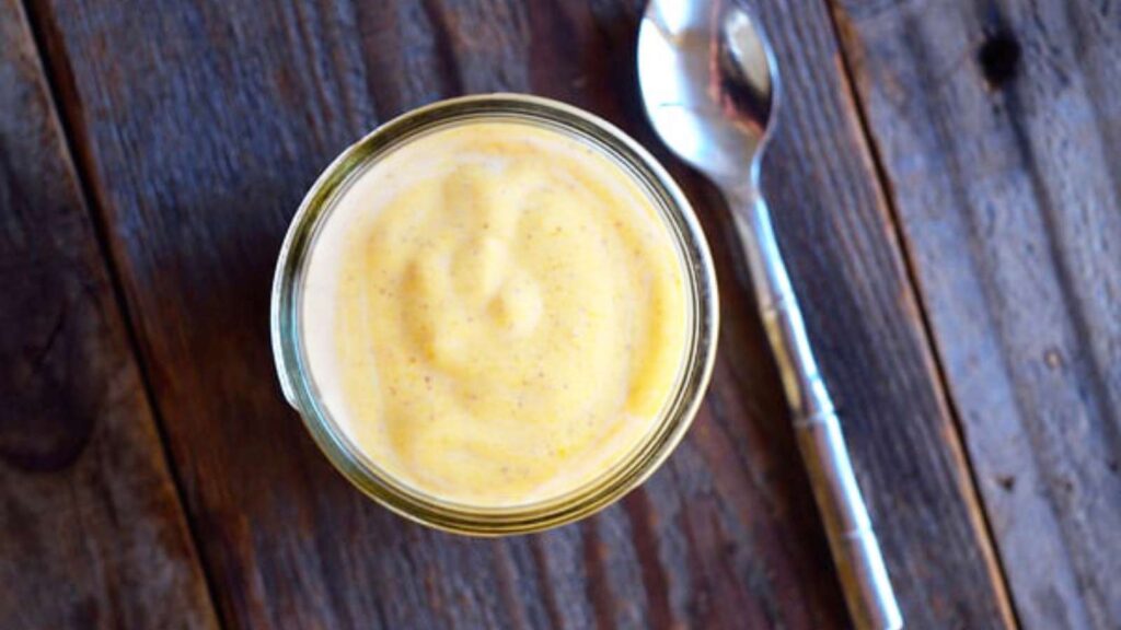 A jar of Pumpkin Pie Yogurt on a wooden tabletop. A spoon lays to the right of the jar.