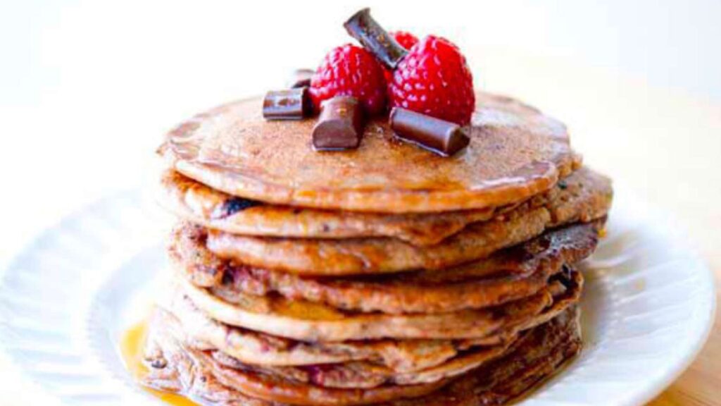 A stack of Raspberry And Dark Chocolate Chip Pancakes on a white plate.