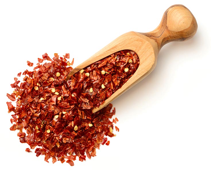 A wooden scoop filled with red chili flakes on a white background.