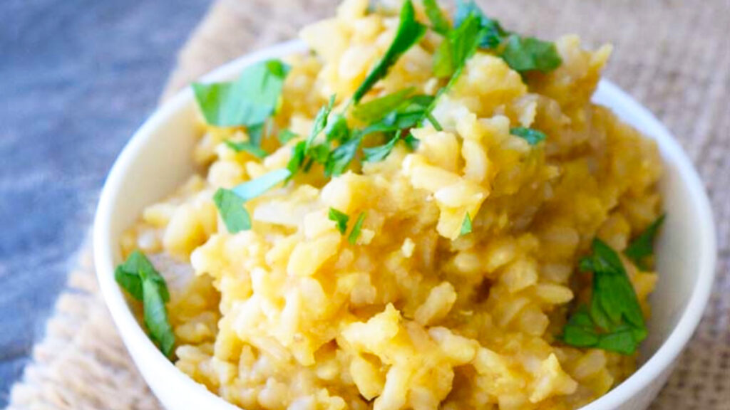 A white bowl on a placemat, filled with red lentil lemon rice and garnished with fresh herbs.