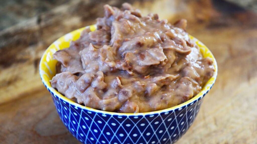 Refried Beans in a small, decorative yellow and blue bowl, sitting on a wood surface.