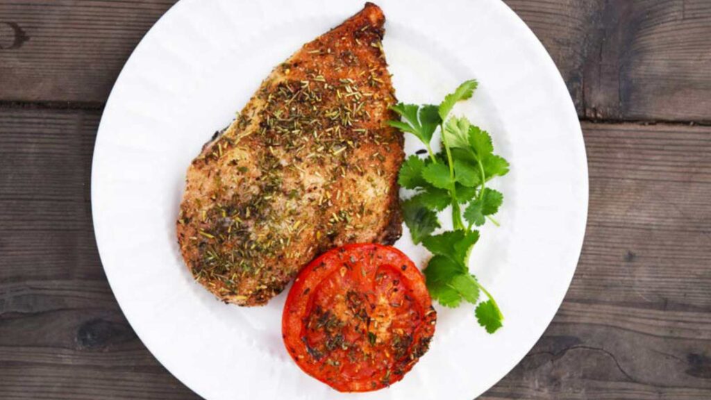A roasted chicken breast and half tomato on a white plate.