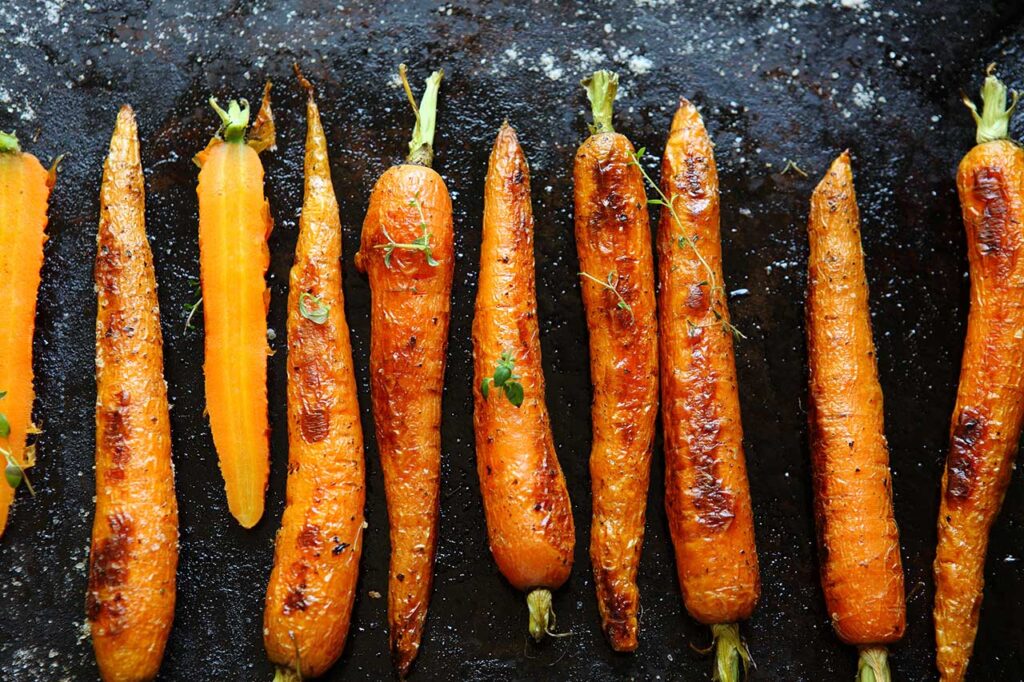 Roasted carrots in a row on a black surface.