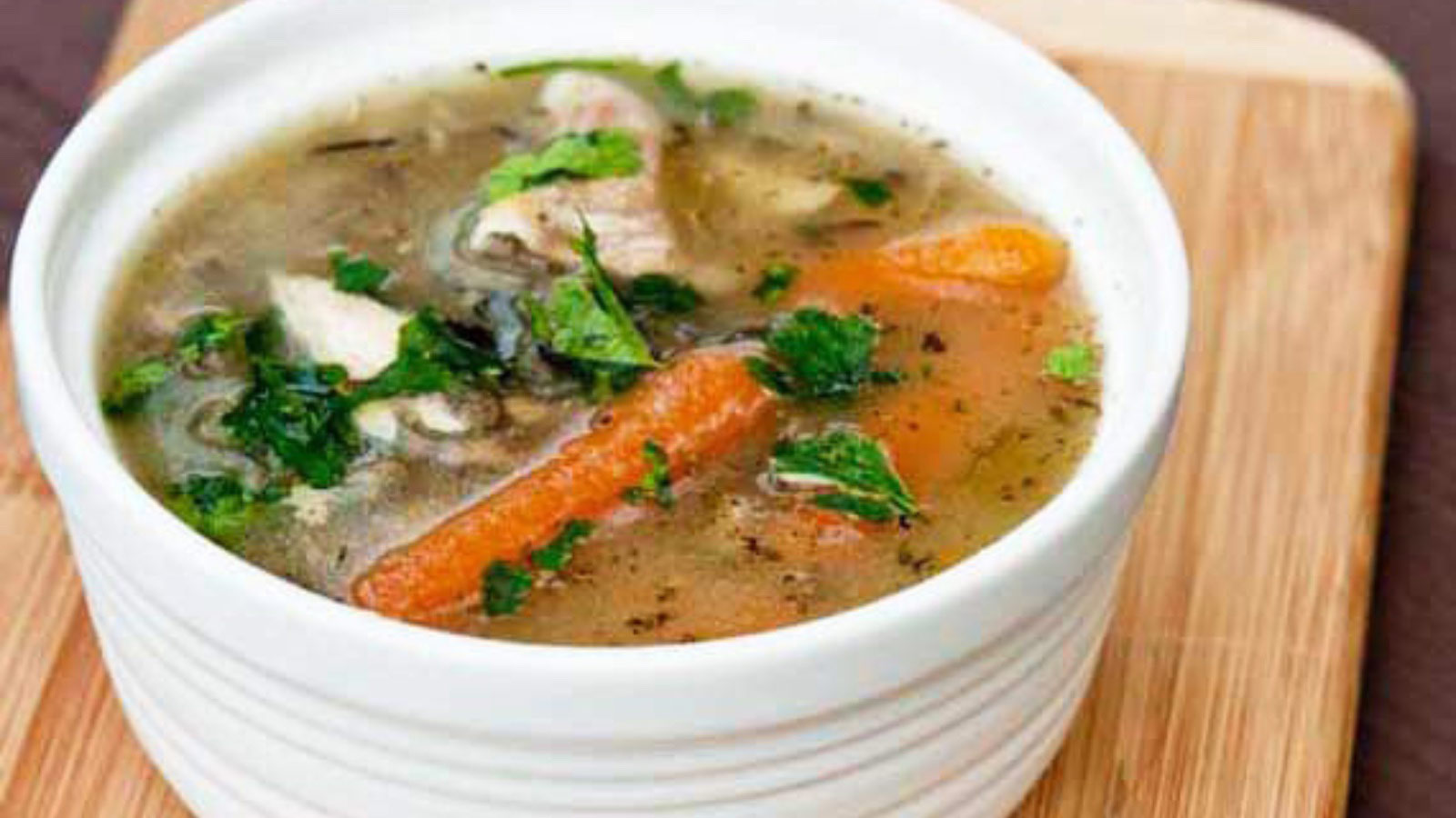 A white bowl filled with Leftover Rotisserie Chicken Soup, sits on a cutting board.