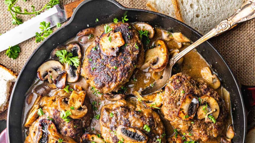 An overhead view of salisbury steak in a skillet.