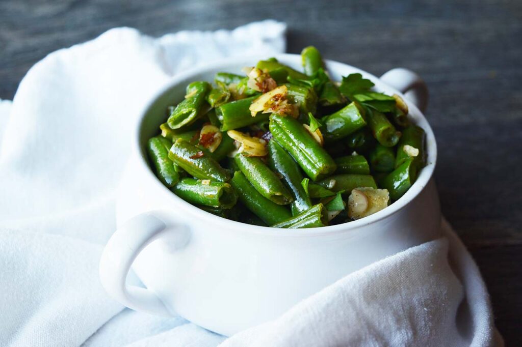 A white crock filled with sautéed green beans and garnished with fresh parsley.