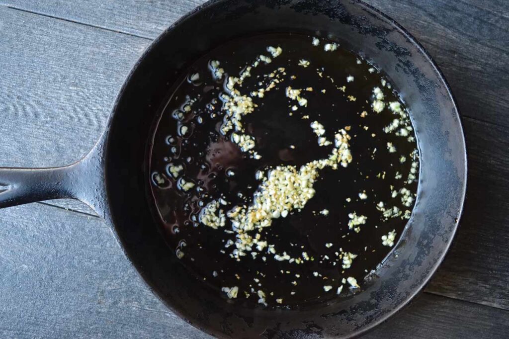 Minced garlic cooking in oil in a cast iron skillet.