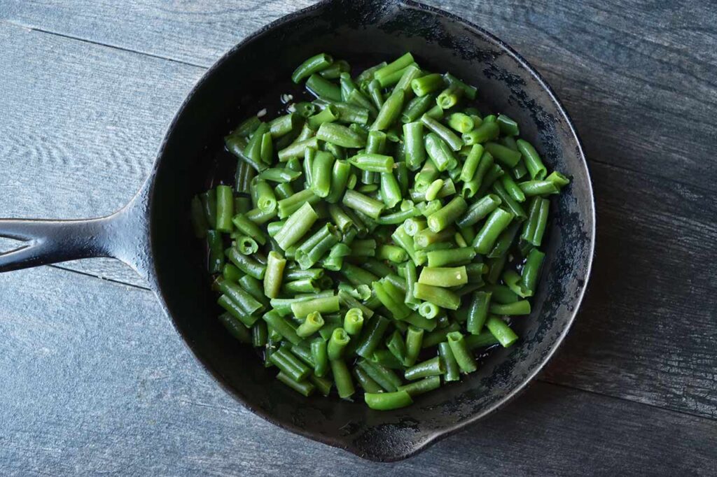 Green beans added to minced garlic in a cast iron skillet.