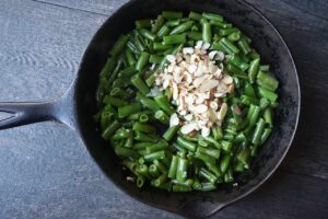 Sliced almonds added to green beans in a skillet.