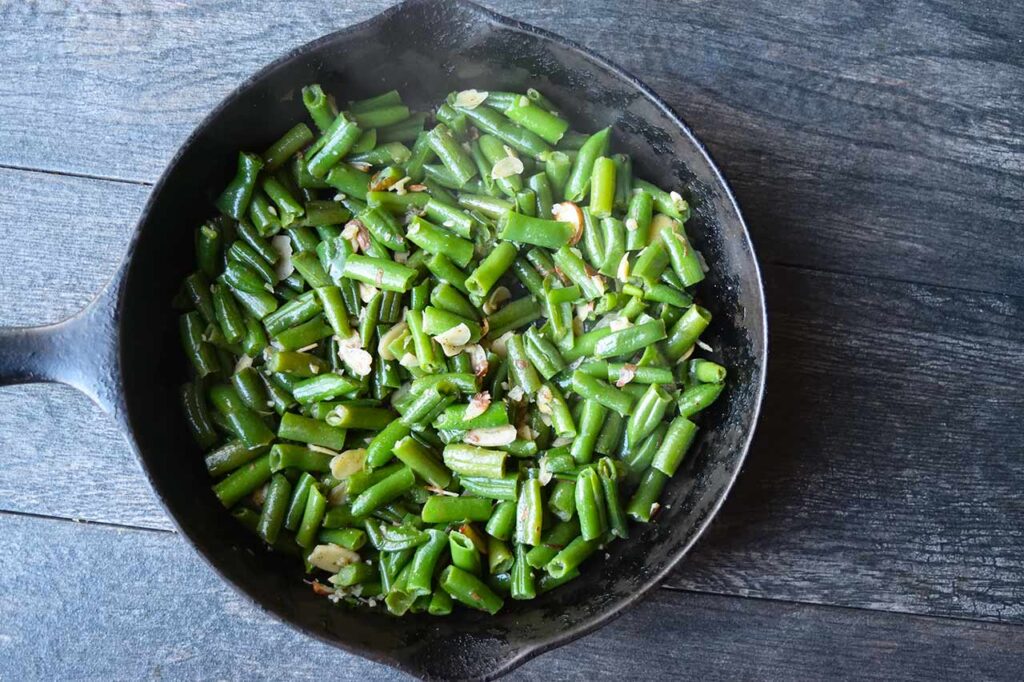 Mixed green beans and sliced almonds with garlic in a skillet.