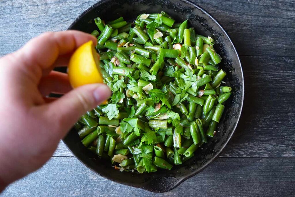 Squeezing half a lemon into a skillet of green beans.