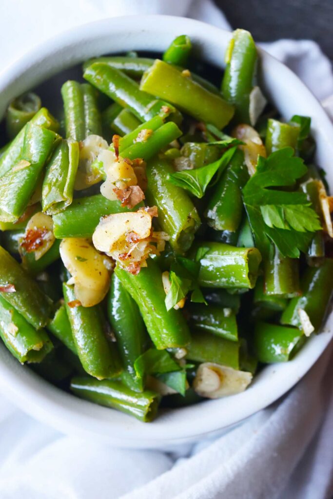 An overhead view of Sautéed Green Beans with almonds in a white crock.