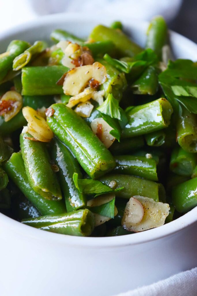 A closeup side view of a white crock filled with Sautéed Green Beans With Almonds.