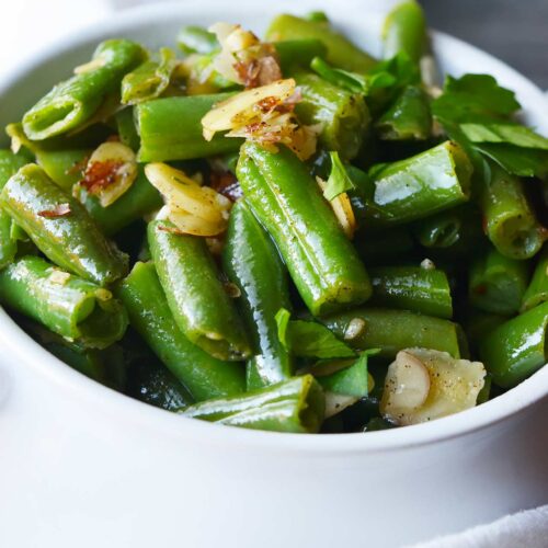 A side view of a white crock filled with Sautéed Green Beans With Almonds.