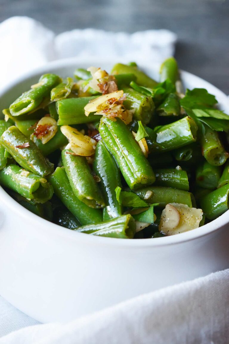 A side view of a white crock filled with Sautéed Green Beans With Almonds.