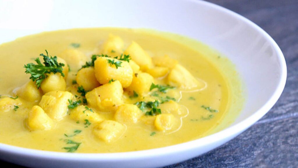 A white bowl on a gray surface, filled with Scallop Soup garnished with fresh parsley.