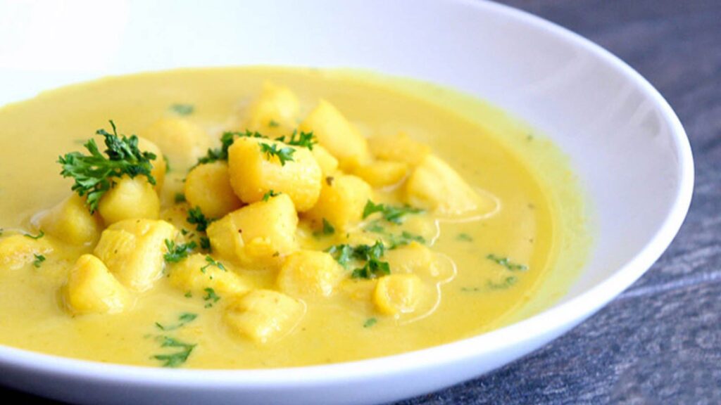 A white bowl on a gray surface, filled with Scallop Soup garnished with fresh parsley.