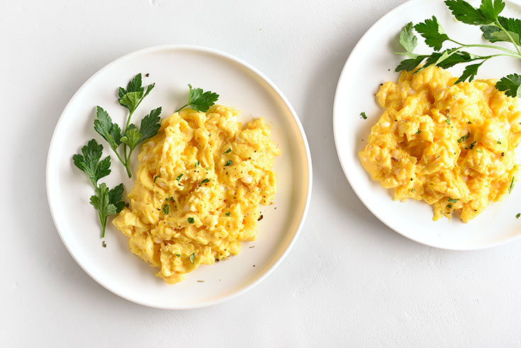 Two white plates, each with a serving of scrambled eggs and a garnish of fresh parsley.