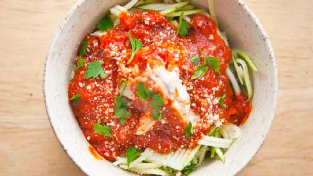 A bowl of baked marinara chicken over a zucchini noodles sitting on a table.
