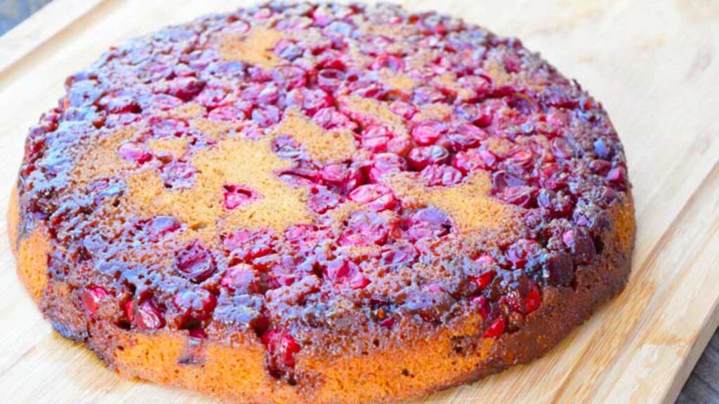 A whole Cranberry Upside Down Cake resting on a wood cutting board.