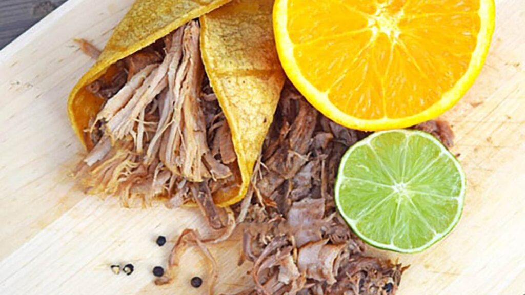 An overhead view looking down on a Slow Cooker Carnita laying on a cutting board with an orange and lime.