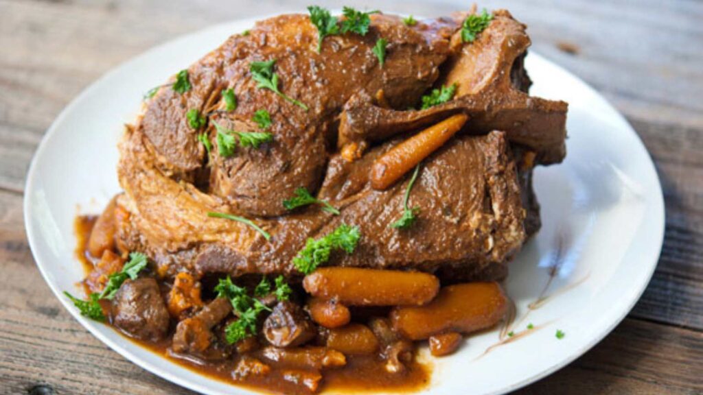 A whole Slow Cooker Pork Roast with carrots on a white platter.