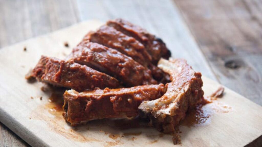 Six ribs lay on a cutting board with sauce on them.