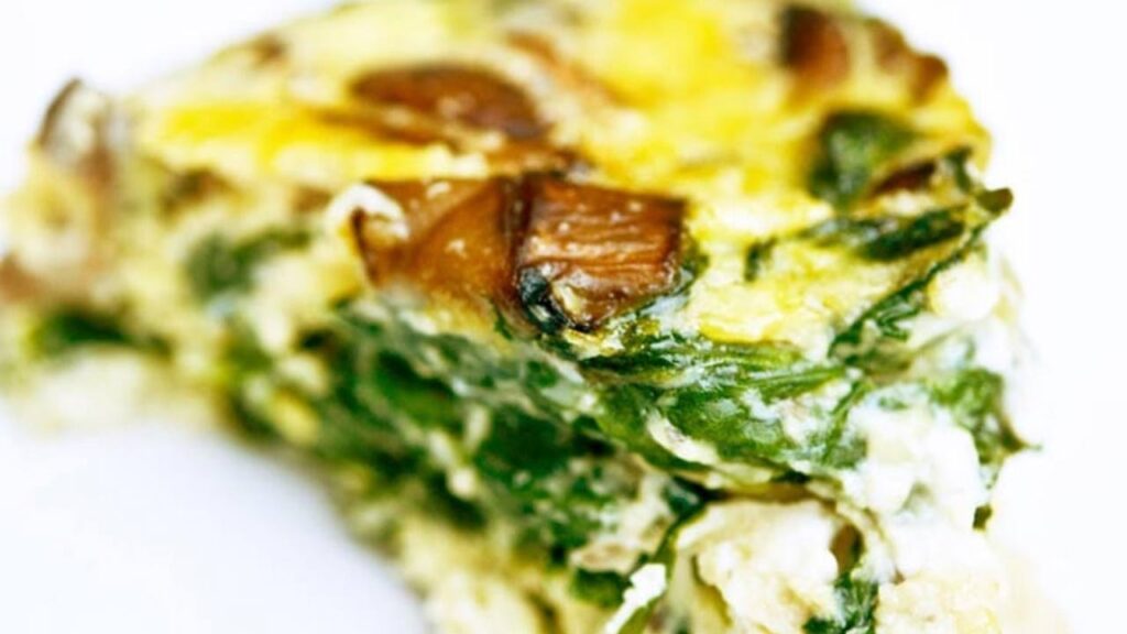 A closeup of a slice of spinach mushroom frittata on a white surface.