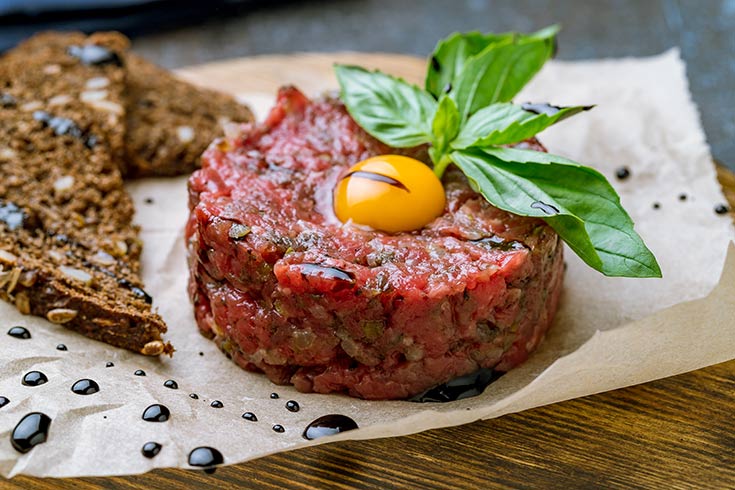 A steak tartare with a raw egg yolk on top sits on a parchment-lined cutting board.