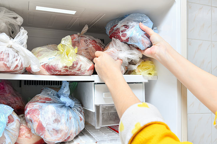 Female hands placing food in a full freezer.