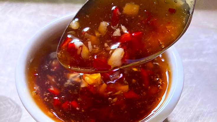 A closeup of a spoon lifting some Thai Sweet Chili Sauce out of a small, white bowl.