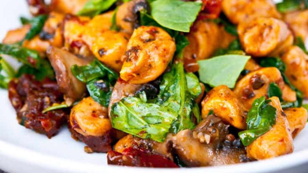 A closeup of Sweet Potato Gnocchi With Mushrooms And Sun Dried Tomatoes in a white bowl.
