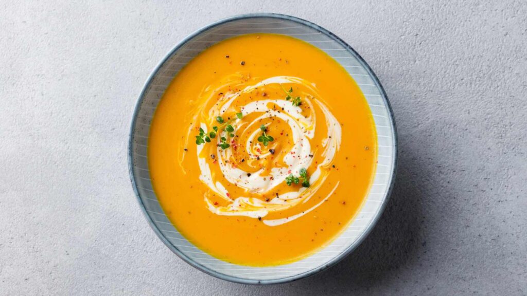 A bowl of sweet potato soup on a gray surface.