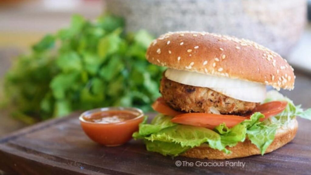 A taco burger sitting on a cutting board next to a small bowl of salsa.